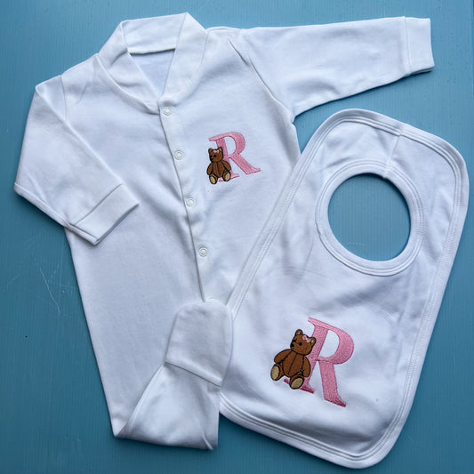 White baby outfit with 'R' and teddy bear design on a blue background