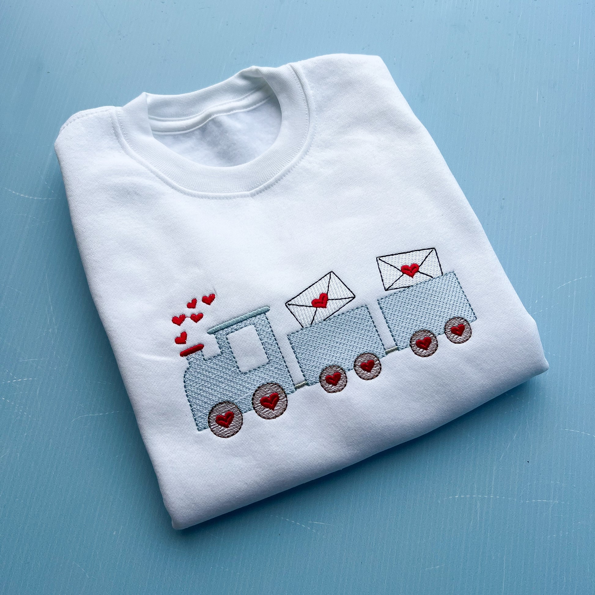 White sweatshirt with a train and love hearts embroidered into the front