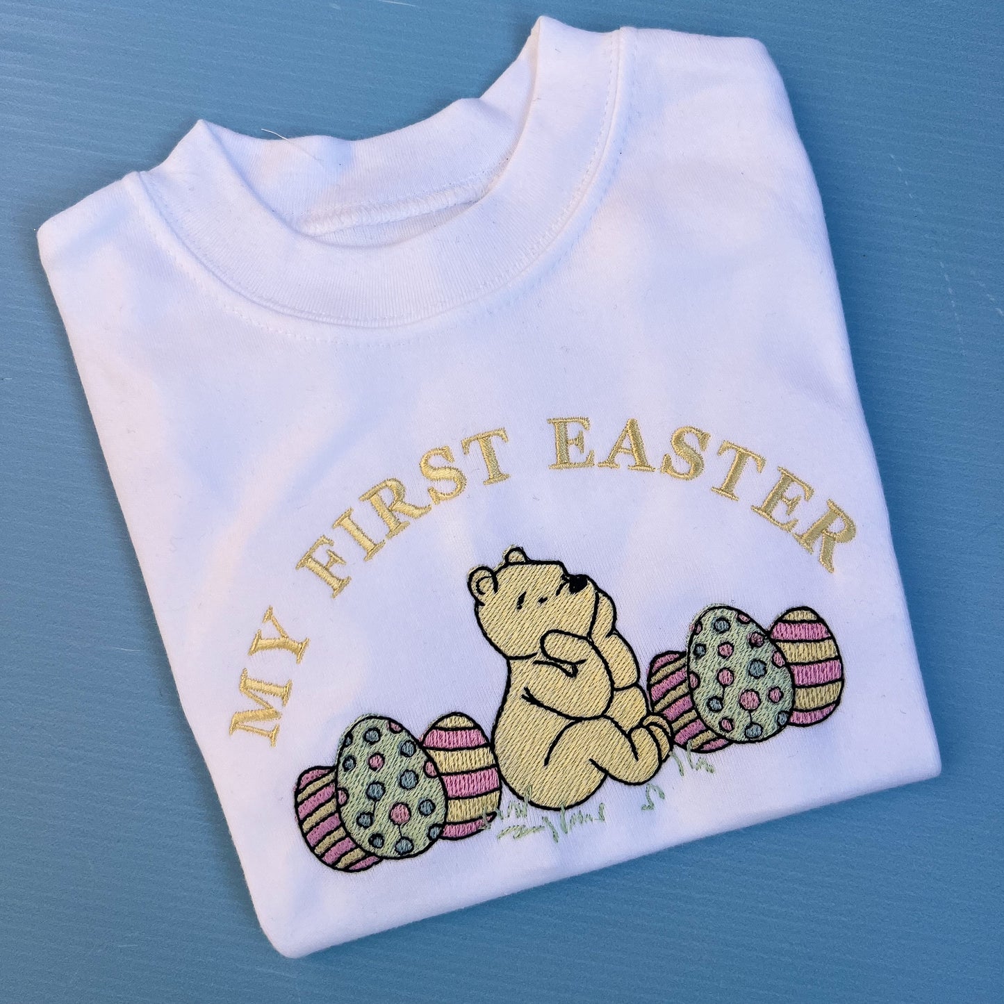Folded white shirt with embroidered text and bear design on a blue background