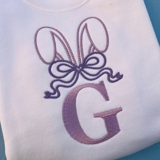 White jumper with embroidered bunny ears, a large bow and the letter G 