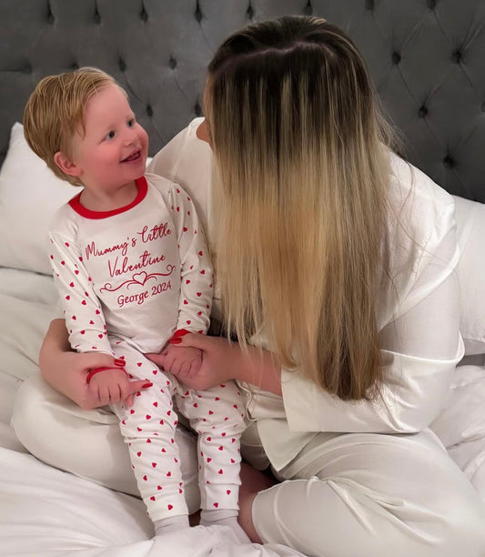 Woman and child in pajamas sitting on a bed, with the woman holding the child's hand.