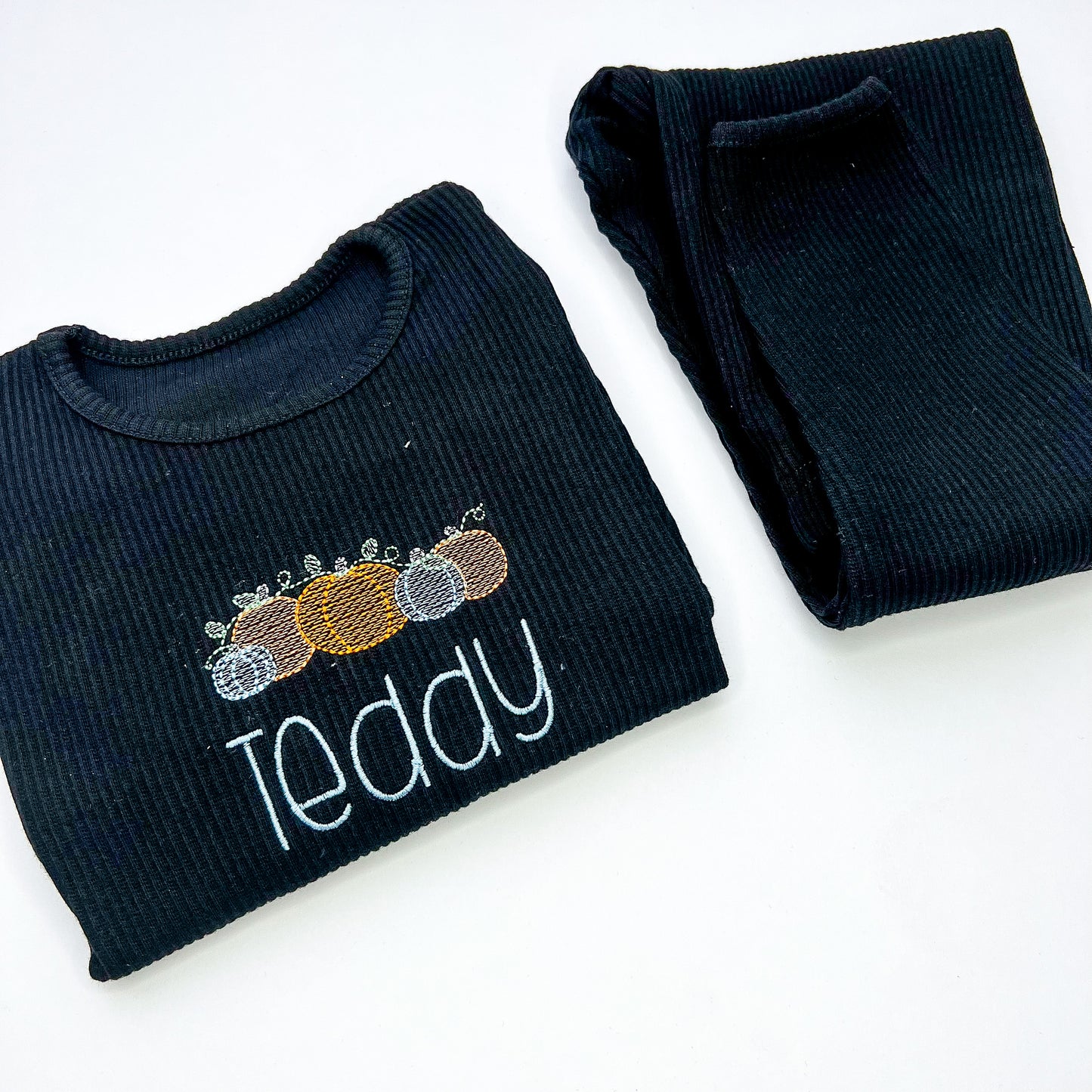 black loungewear with 5 embroidered pumpkins, 3 orange and 2 blue and childs name in blue